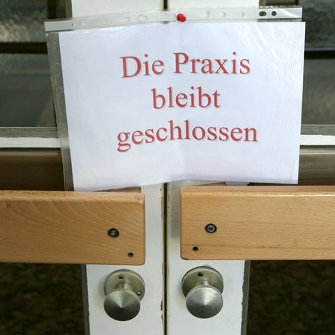 An einer Tür zu einer Arztpraxis hängt ein Schild mit der Aufschrift «Die Praxis bleibt geschlossen».