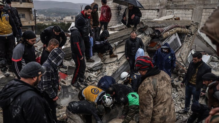 Syrische Zivilisten und Mitglieder der Weißhelme arbeiten an der Rettung von Menschen, die nach einem Erdbeben der Stärke 7,8 in Syrien unter einem zerstörten Gebäude eingeschlossen sind.