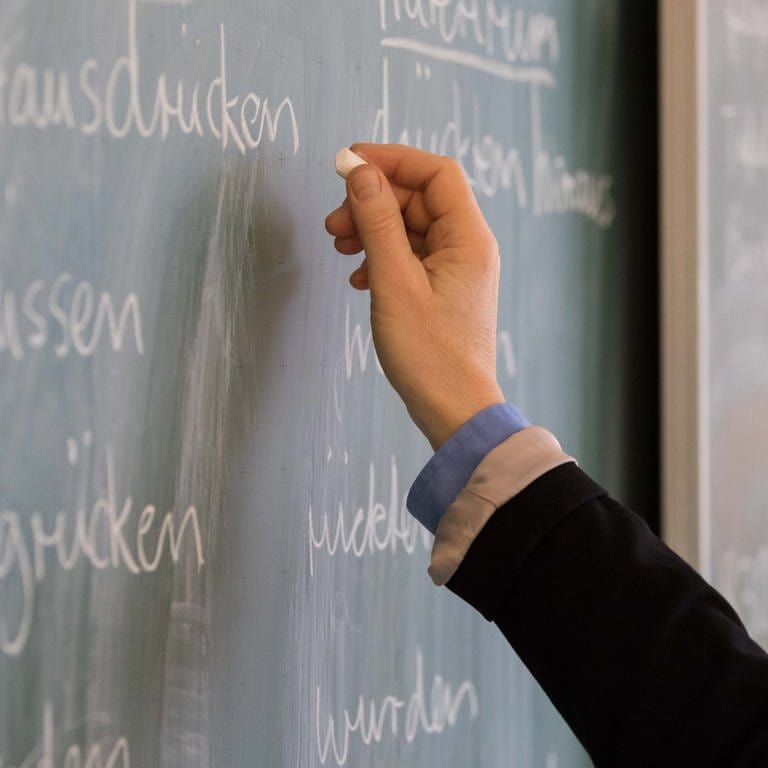 Ein Lehrer steht in einem Klassenraum an einer Tafel und schreibt.
