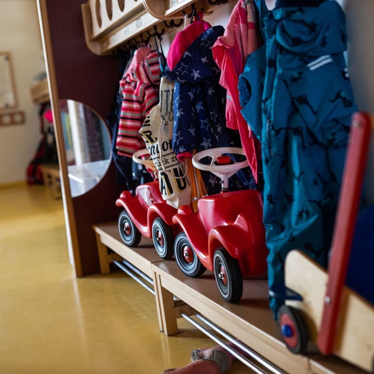 Bobbycars stehen unter Jacken von Kindern, die an einer Garderobe einer Kindertagesstätte (Kita) hängen. 