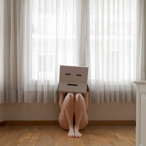 Frau versteckt sich hinter Box wegen Körperstandards auf Social Media. Das kann Essstörungen verursachen. (Foto: IMAGO, Westend61)