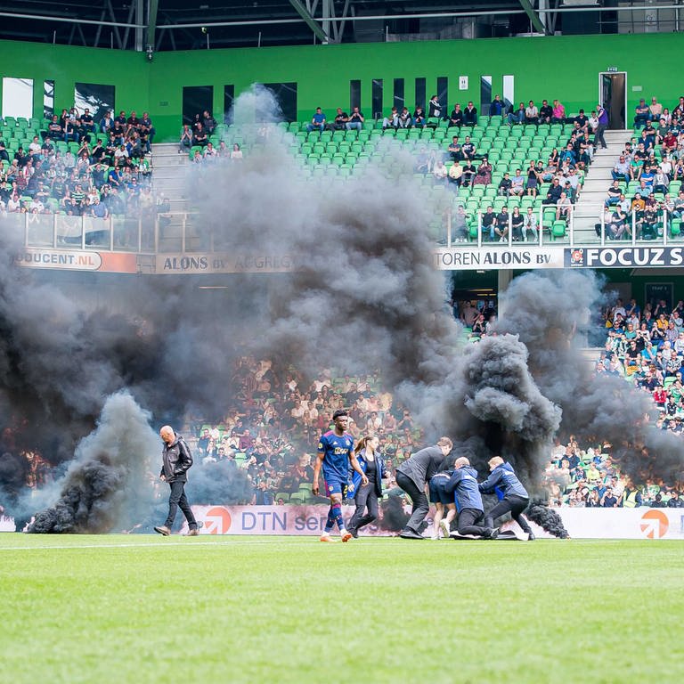 Fußball: Ehrendivision, Niederlande, Hauptrunde, 32. Spieltag, FC Groningen - Ajax Amsterdam: Fans des FC Groningen werfen während des Spiels Rauchbomben auf das Spielfeld und einige Fans, die auf das Spielfeld gelaufen sind, werden von Ordnern festgehalten. (Foto: dpa Bildfunk, picture alliance/dpa/ANP | Cor Lasker)