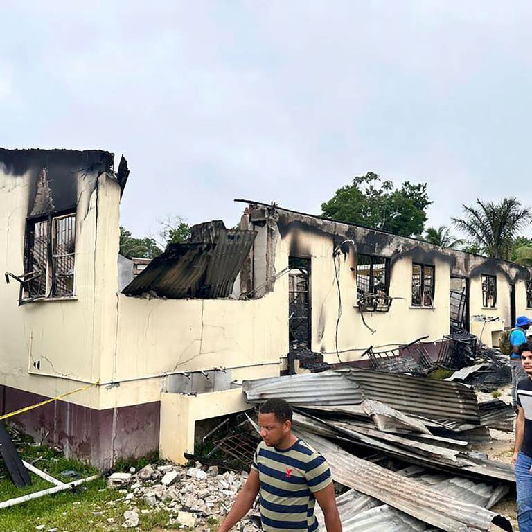 Menschen stehen vor dem ausgebrannten Schlafsaal einer Schule. Bei einem Brand in einem Schlafsaal an einer Schule im südamerikanischen Guyana sind 19 Menschen gestorben. (Foto: dpa Bildfunk, picture alliance/dpa/Guyana's Department of Public Information/AP | -)