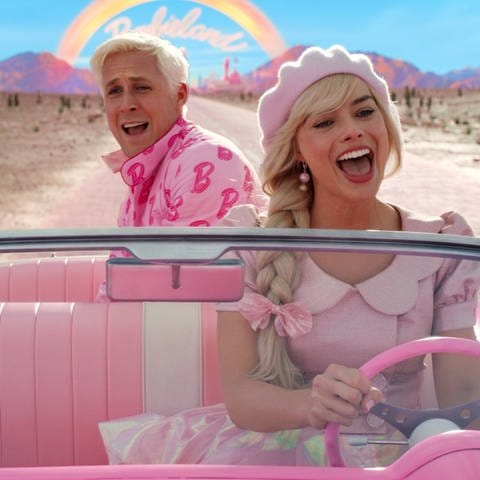Barbie (Margot Poppie) und Ken (Ryan Gosling) fahren in einem pinken Auto.