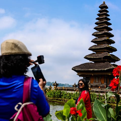 Ein Tourist macht ein Foto von einer Touristin vor einem Tempel auf Bali, Indonesien.