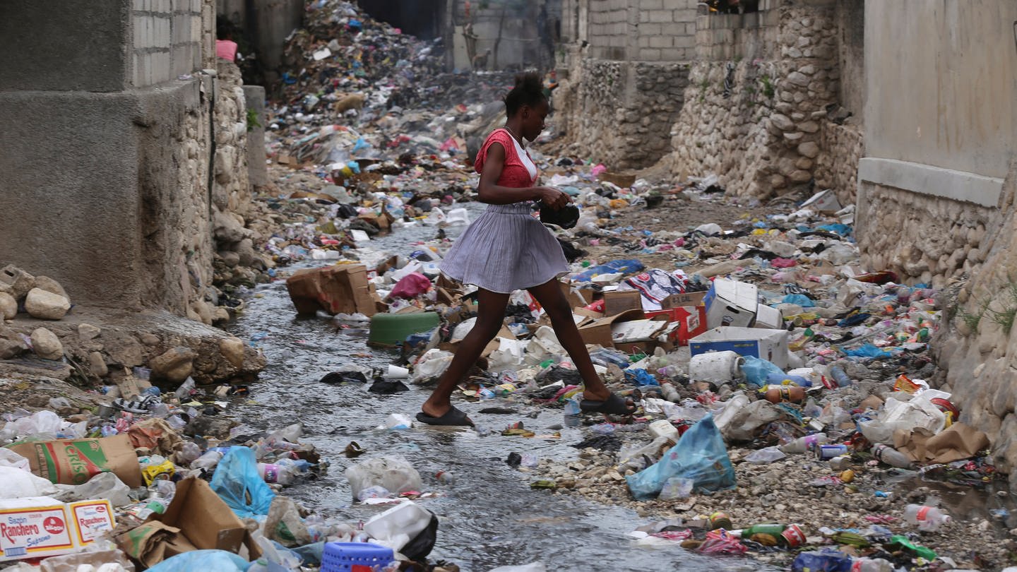 Ein Mädchen geht in einem Viertel von Parc-Au-Price durch eine Häuserschlucht, die voller Müll ist. Hier ist Armut allgegenwärtig. (Foto: dpa Bildfunk, picture alliance/dpa/AP | Odelyn Joseph)