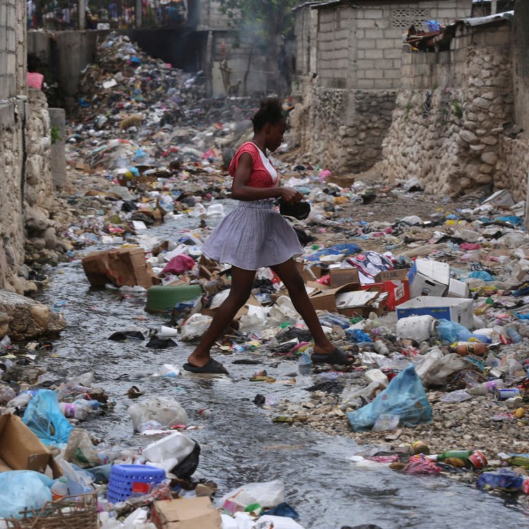 Ein Mädchen geht in einem Viertel von Parc-Au-Price durch eine Häuserschlucht, die voller Müll ist. Hier ist Armut allgegenwärtig.