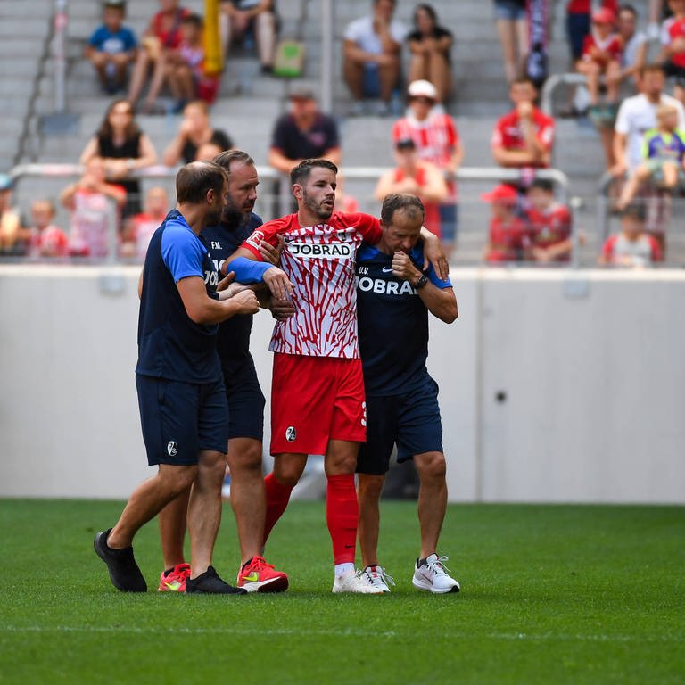 Christian Günter wird mit einem gebrochenen Arm vom Feld begleitet (Foto: IMAGO, IMAGO / Beautiful Sports)