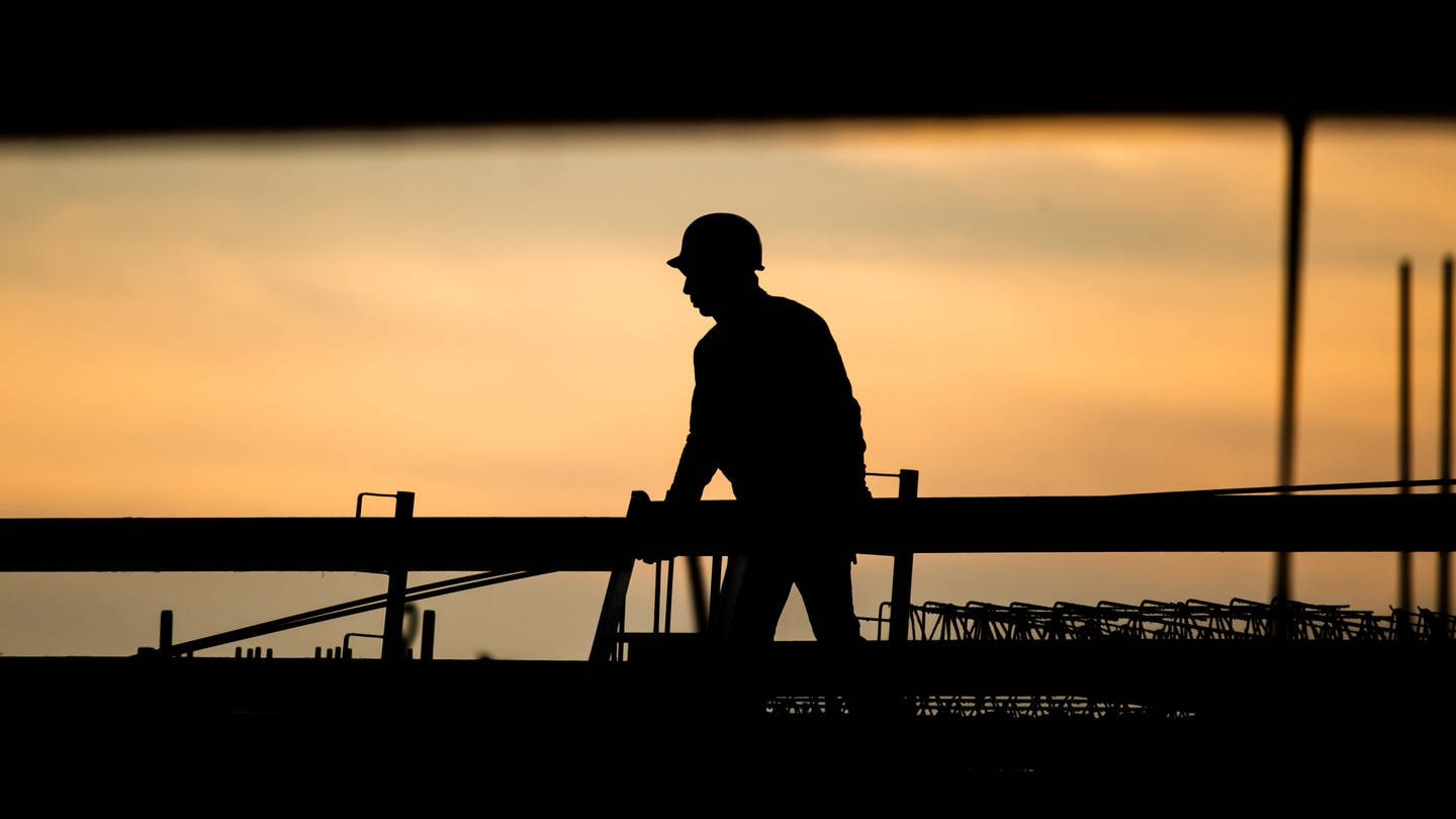 Die Silhouette eines Bauarbeiters zeichnet sich auf einer Baustelle vor dem verfärbten Morgenhimmel ab. Der Fachkräftemangel stellt die deutsche Wirtschaft vor große Herausforderungen. (Foto: dpa Bildfunk, picture alliance/dpa | Julian Stratenschulte)