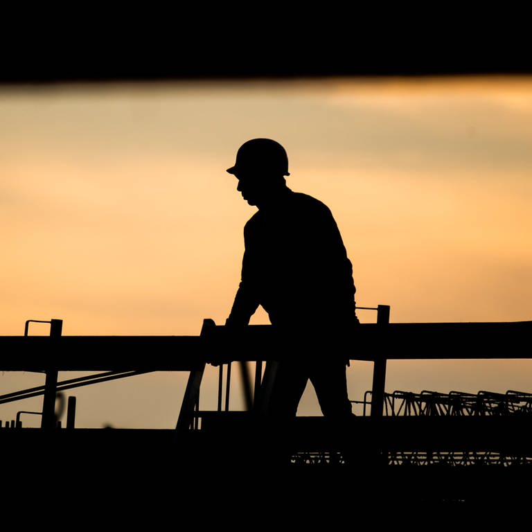 Die Silhouette eines Bauarbeiters zeichnet sich auf einer Baustelle vor dem verfärbten Morgenhimmel ab. Der Fachkräftemangel stellt die deutsche Wirtschaft vor große Herausforderungen. (Foto: dpa Bildfunk, picture alliance/dpa | Julian Stratenschulte)