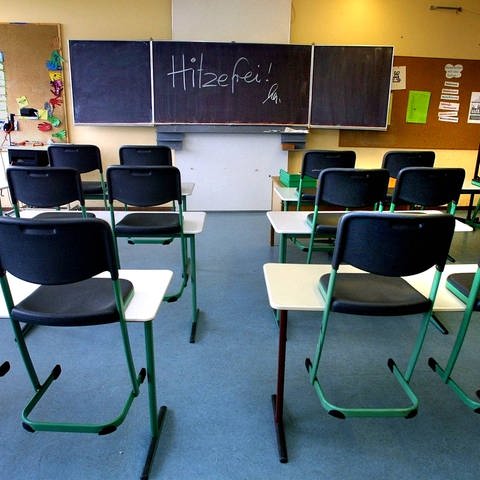 Ein leeres Klassenzimmer in einer Schule. Auf der Tafel steht "Hitzefrei".
