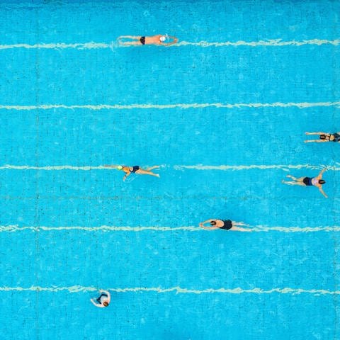 Menschen schwimmen ihre Bahnen in einem Schwimmbad (Symbolfoto).