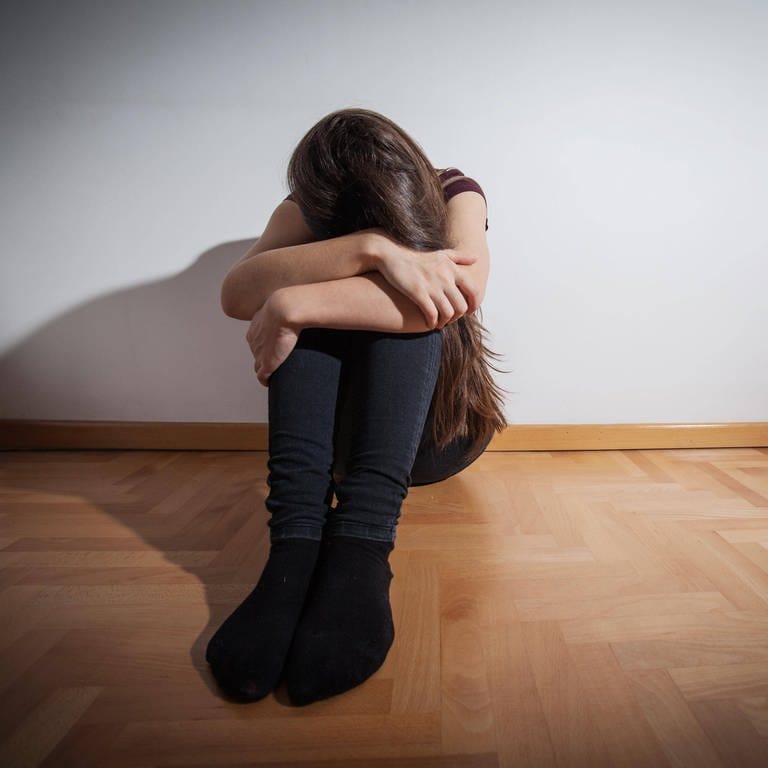 Mädchen mit Depression verschränkt die Arme über dem Kopf