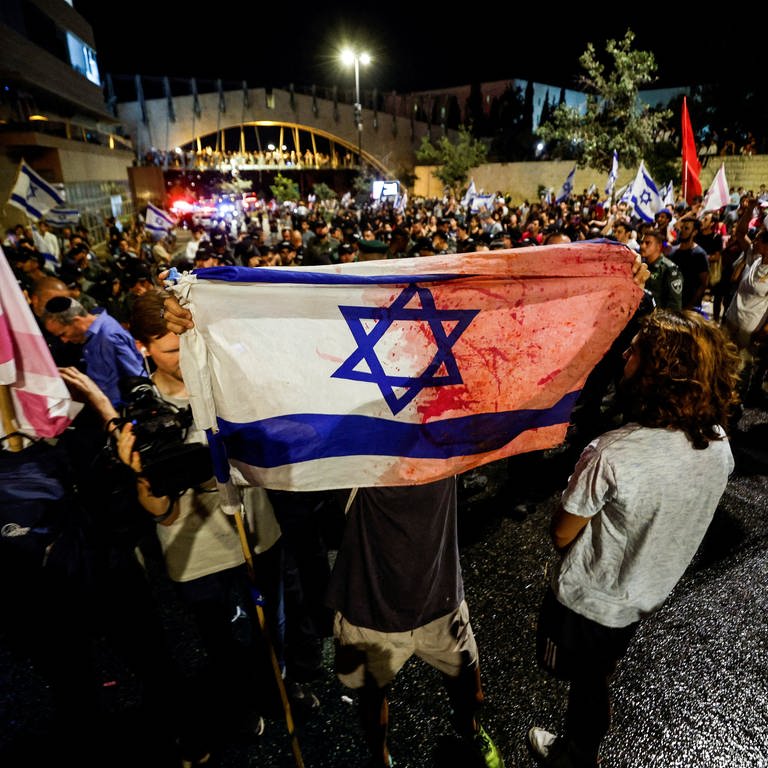 Ein Demonstrant hält während der Proteste gegen die Justizreform in Israel eine Israel-Flagge, die mit roter Farbe wie Blut bespritzt wurde.