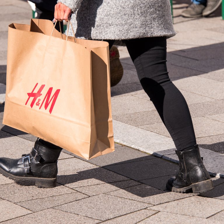 Eine junge Frau läuft nach dem Shopping mit einer Papiertüte der schwedischen Modemarke H&M durch eine Einkaufsstraße.