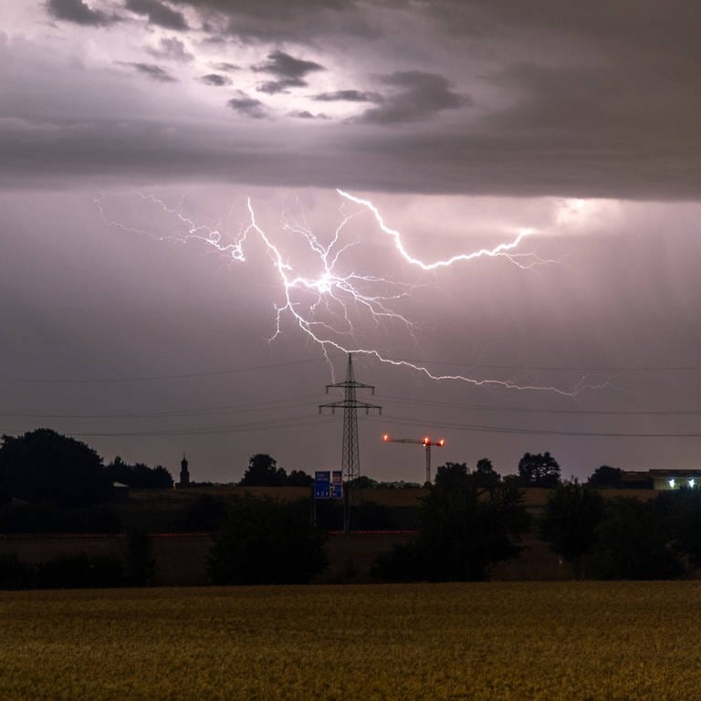 Ein Blitz ist hinter einem Strommast zu sehen. (Symbolbild) (Foto: IMAGO, Jan Eifert (Symbolbild))