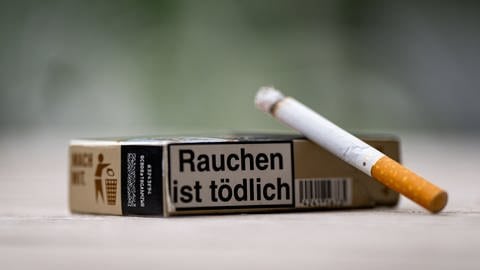 Eine Zigarette vor einer Packung, auf der "Rauchen ist tödlich" steht - Herzinfarkt vorbeugen
