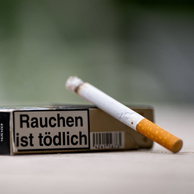 Eine Zigarette vor einer Packung, auf der "Rauchen ist tödlich" steht