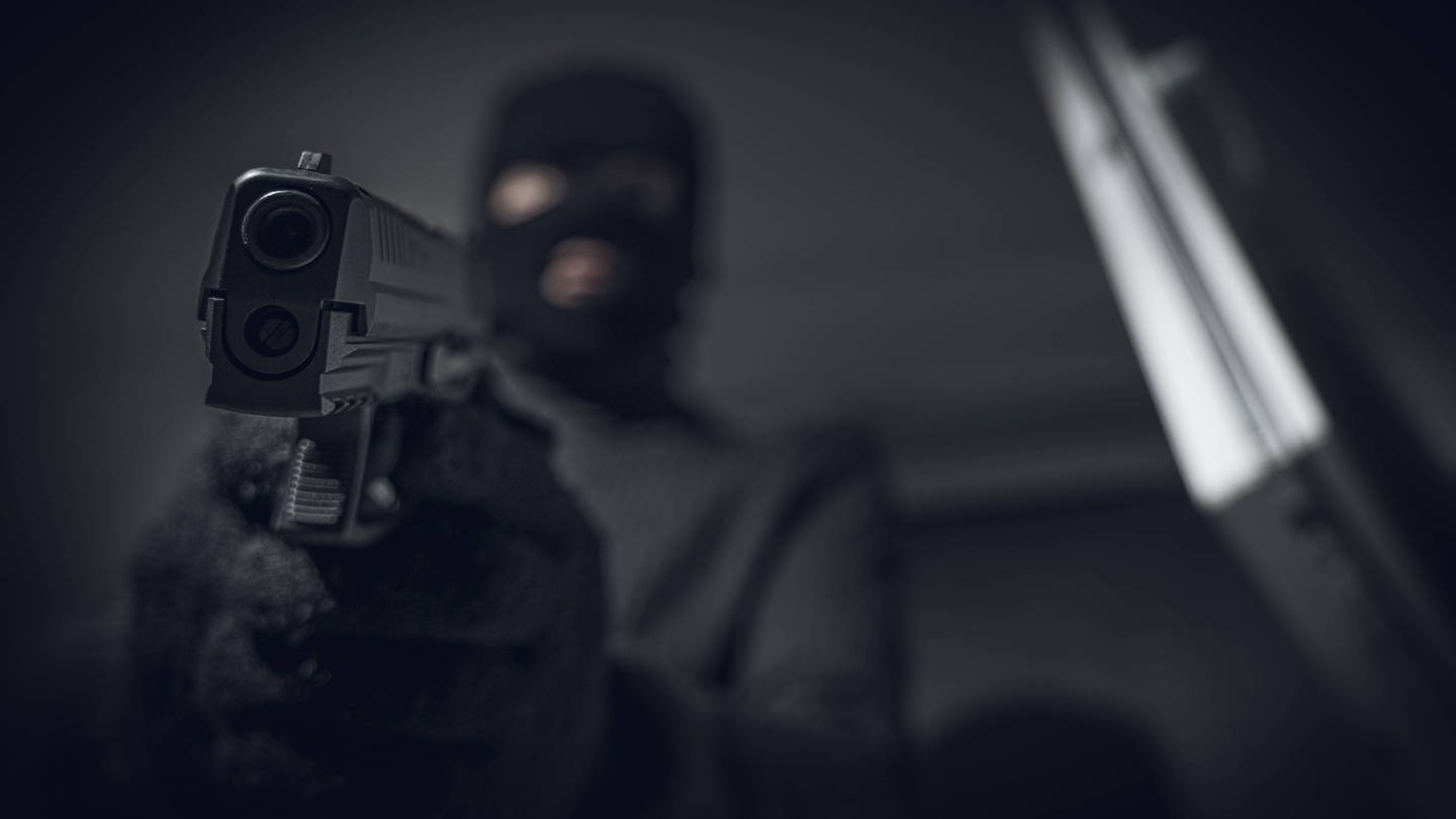 Ein Maskierter hält eine Pistole in die Kamera (Foto: IMAGO, IMAGO/Bihlmayerfotografie)
