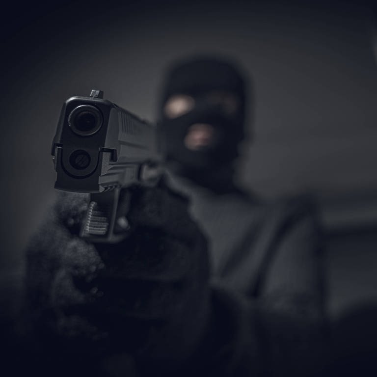 Ein Maskierter hält eine Pistole in die Kamera (Foto: IMAGO, IMAGO/Bihlmayerfotografie)
