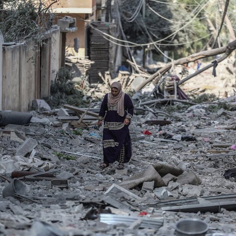 Eine Frau geht durch das Karama-Viertel nach einem israelischen Luftangriff. (Foto: dpa Bildfunk, picture alliance/dpa | Mohammed Talatene)