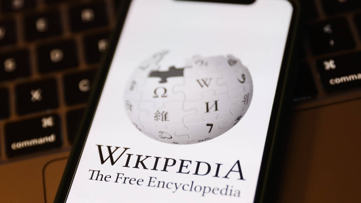 Das Wikipedia-Logo auf einem Handybildschirm und einer Laptoptastatur; Wikipedia will mit Künstlicher Intelligenz besser werden (Foto: IMAGO, IMAGO / NurPhoto)