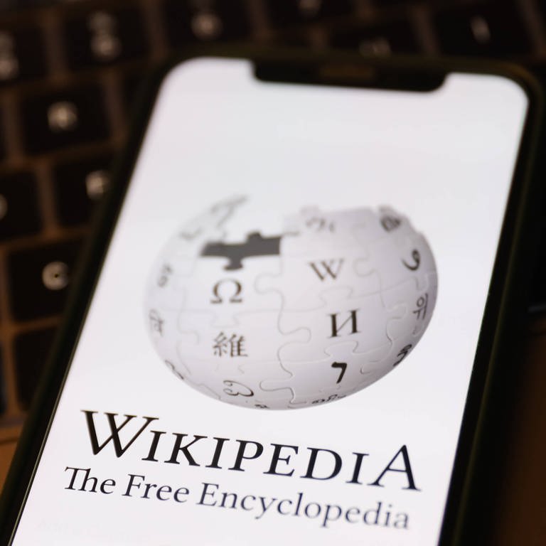 Das Wikipedia-Logo auf einem Handybildschirm und einer Laptoptastatur; Wikipedia will mit Künstlicher Intelligenz besser werden