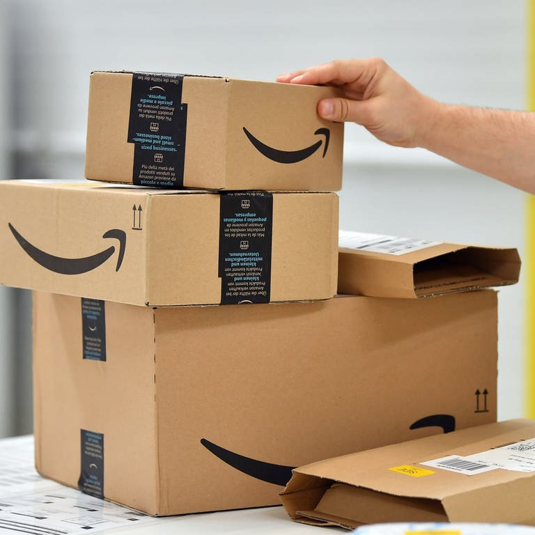Im "Shopfloor" des Amazon Verteilzentrums für Pakete und Päckchen stehen Paket-Sendungen auf einem Tisch. Die EU-Komission hat ein Prüfverfahren gegen Amazon eingeleitet (Symbolbild)