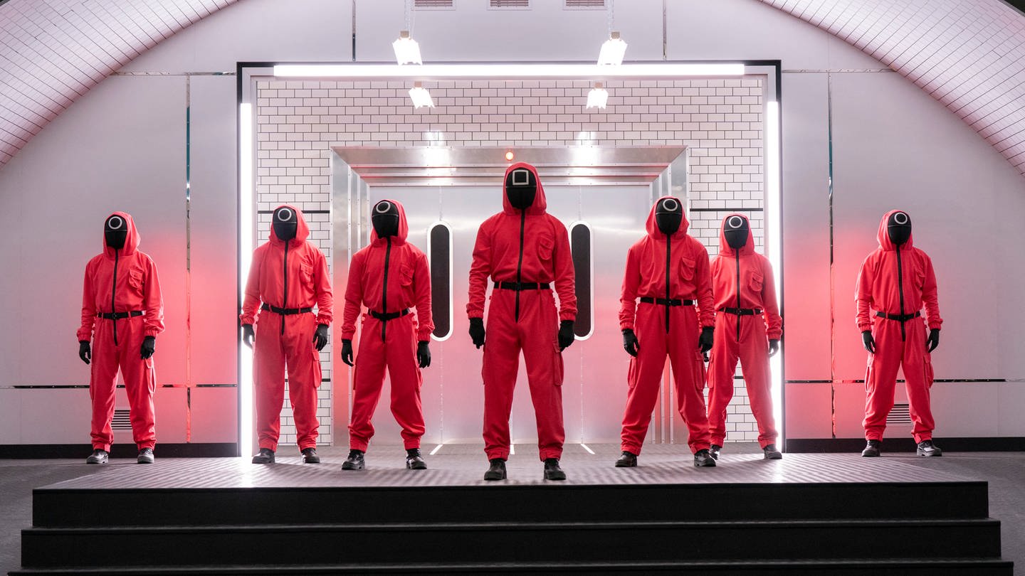 Charaktere der Serie «Squid Game: The Challenge» stehen in roten Anzügen und Masken nebeneinander. Netflix hat mitgeteilt, dass es eine zweite Staffel der Show geben wird. (Foto: dpa Bildfunk, picture alliance/dpa/Netflix | Pete Dadds)