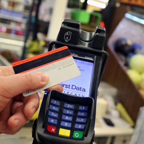 Eine EC-Karte wird an den Bezahl-Terminal an der Kasse eines Supermarktes gehalten.