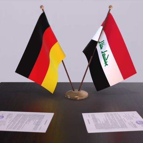 Die Flaggen von Deutschland und dem Irak stejem auf einem Tisch. Angeblich gibt es einen geheimen Deal zwischen beiden Ländern. Es geht unter anderem um Abschiebungen.