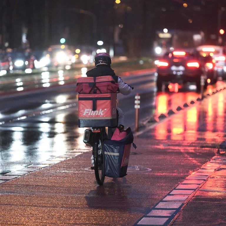 Lieferdienst-Fahrer von Flink unterwegs auf einer nassen Straße im Dunkeln: Die EU will die Rechte der Liefer- und Fahrdienste stärken.