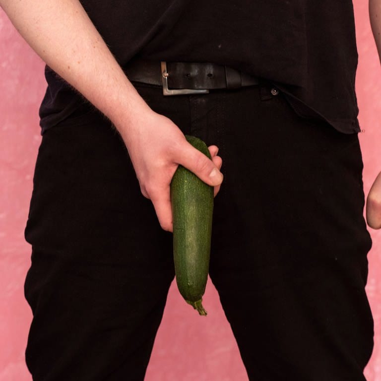 Ein Mann hält eine Zucchini als Penis an seine Hose. Bei einer Studie wurde festgestellt, dass es einen Zusammenhang zwischen Weihnachten und Penisbrüchen gibt.