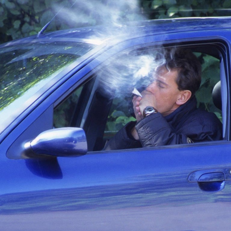 Junger Mann raucht in seinem Auto einen Joint: Bundesregierung plant Strafen für Cannabiskonsum beim Auto fahren.