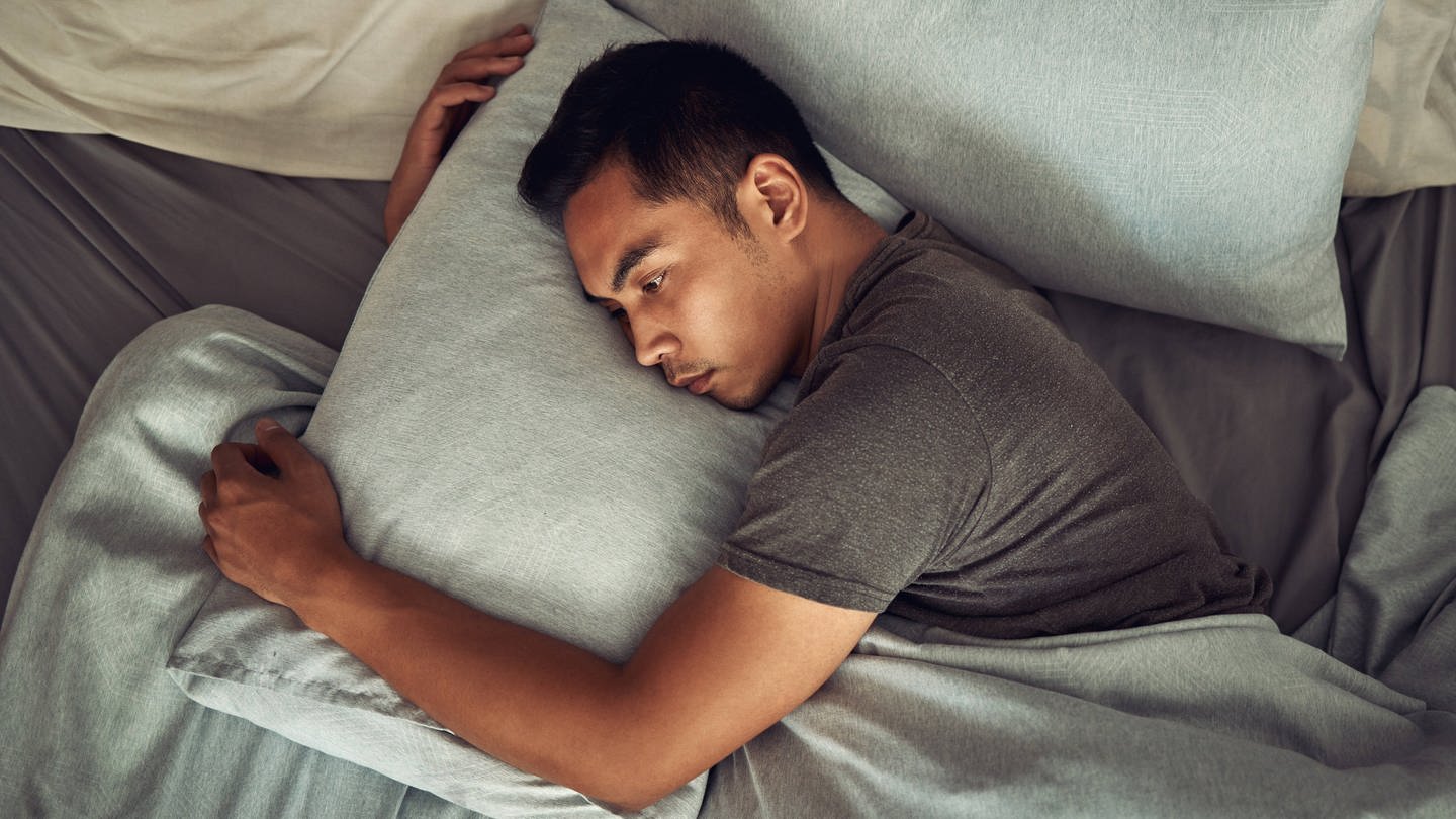 Junger Mann liegt wach im Bett - Fällt es dir schwer, zu entspannen oder zu schlafen. Du bist nicht allein! Das hat jetzt eine neue Umfrage ergeben. (Foto: IMAGO, IMAGO / Zoonar)