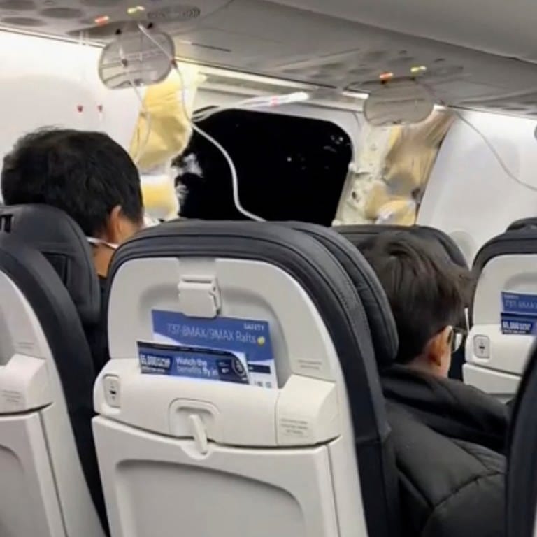 Dieses Bild aus einem von Elizabeth Le zur Verfügung gestellten Video zeigt Passagiere, die in einer Boeing 737-9 Max in der Nähe des abgerissenen Kabinenteils samt Fenster sitzen.  (Foto: dpa Bildfunk, picture alliance/dpa/Elizabeth Le | Elizabeth Le)