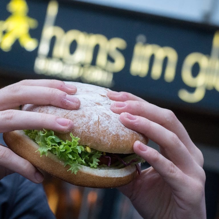 Eine junge Frau hält einen Burger der Burger-Kette "Hans im Glück". - Ein geheimes Treffen von AfD-Politikern mit Neonazis und Unternehmern hat erste Konsequenzen. Die Restaurantkette "Hans im Glück" hat sich mit sofortiger Wirkung von ihrem Mitinhaber Hans-Christian Limmer getrennt.