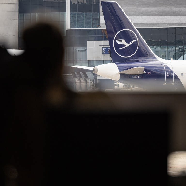 Blick auf das Heck einer Lufthansa Maschine, im Vordergrund sind zwei Personen. - Am Mittwoch will das Bodenpersonal der Lufthansa streiken.