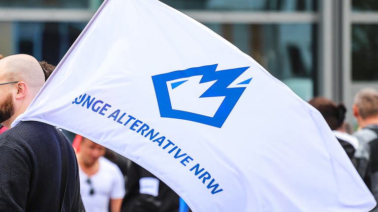 Ein Mitglied der «Jungen Alternative» (JA), Jugendorganisation der AfD, trägt auf einer Wahlkampfveranstaltung eine Fahne mit dem Logo der Organisation. Der nordrhein-westfälische Verfassungsschutz hat die Jugendorganisation der AfD in Nordrhein-Westfalen als rechtsextremistischen Verdachtsfall eingestuft