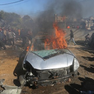Palästinenser sehen zu wie ein Auto brennt, das von einem israelischen Luftangriff im südlichen Gazastreifen getroffen wurde. (Foto: dpa Bildfunk, picture alliance/dpa/AP | Hatem Ali)