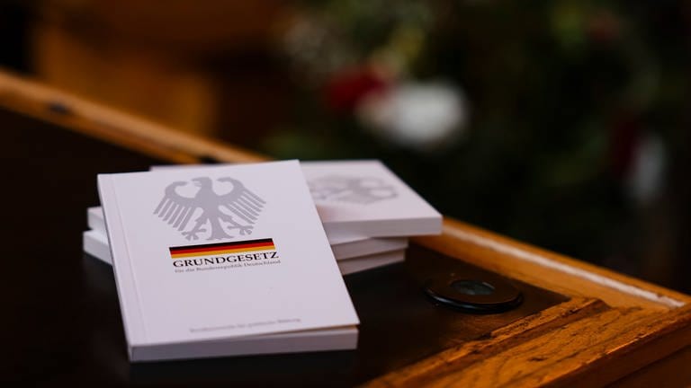 Vier Bücher mit dem Grundgesetz liegen auf einem Tisch. Die Ampel wird Begriff "Rasse" laut einem Bericht doch nicht aus Grundgesetz streichen