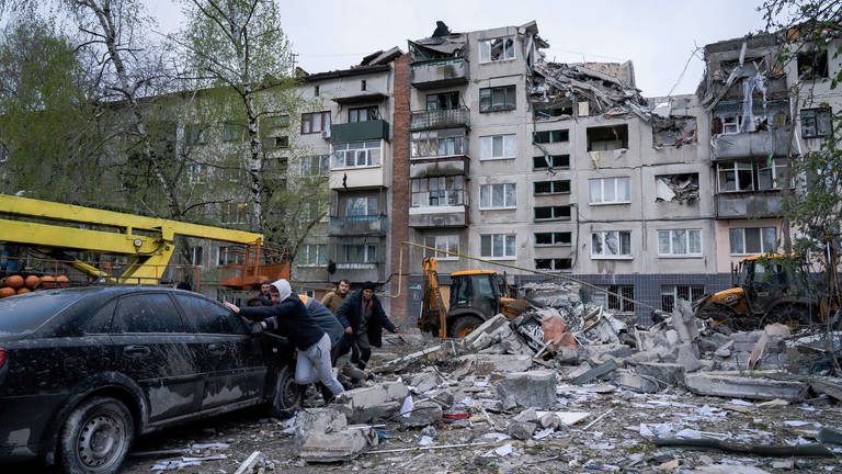 Anwohner schieben ein beschädigtes Auto weg. Bei einem russischen Raketenangriff wurden Gebäude in der Ukrain zerstört. (Foto: dpa Bildfunk, picture alliance/dpa/SOPA Images via ZUMA Press Wire | Ashley Chan)
