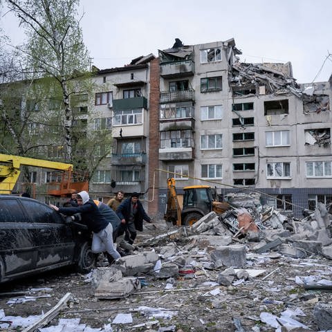 Anwohner schieben ein beschädigtes Auto weg. Bei einem russischen Raketenangriff wurden Gebäude in der Ukrain zerstört.