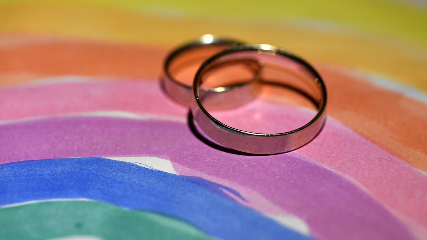 Zwei Eheringe auf einer gemalten Regenbogenfahne - In Griechenland gibt es jetzt auch die Ehe für alle (Foto: dpa Bildfunk, picture alliance / Ralf Hirschberger/dpa-Zentralbild/dpa | Ralf Hirschberger)