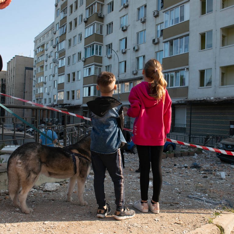 Kinder stehen vor einem beschädigten Gebäude in der Ukraine - Save the Children berichtet von über 600.000 Kindern in Not nach Rückkehr in die Ukraine