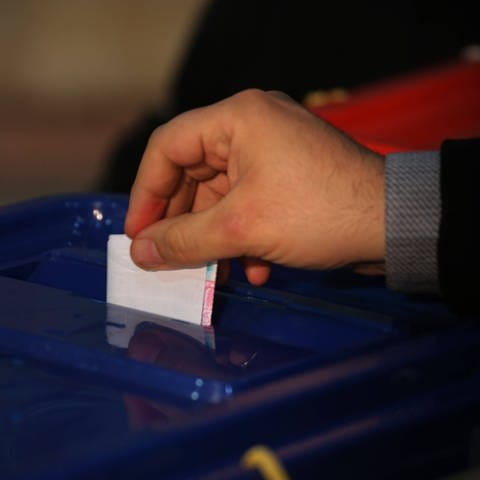 Eine Hand wird einen Wahlzettel in die Urne - Im Iran fand die erste offizielle Wahl seit den Massenprotesten im Jahr 2022 statt.