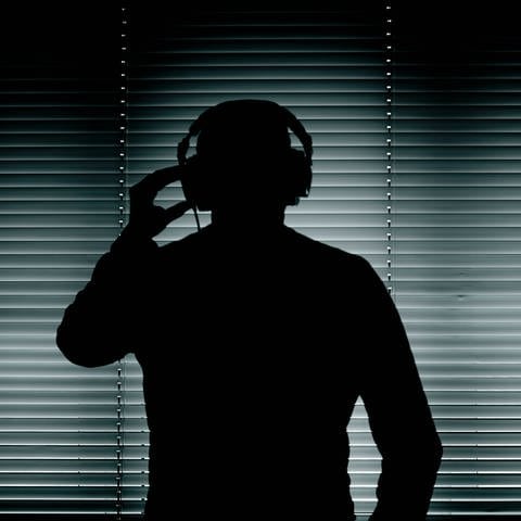 Mann mit Kopfhörer vor einem Fenster mit geschlossenen Jalousien (Symbolfoto)