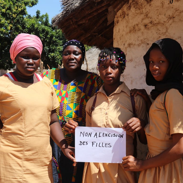 In September 2022, Koulako, 39, poses with her daughters and a sign that reads ‘No to the excision of girls’, at their home in the commune of Damaro in the Kankan region of Guinea. (Foto: UNICEF 2024)