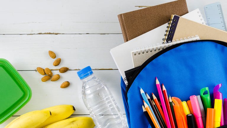 Symbolbild: Eine Schultasche mit Wasser, Banane, Nüssen und Stiften. (Foto: Bild von Freepik)
