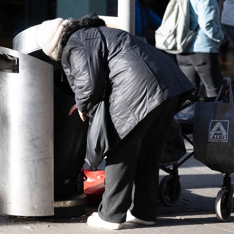 Eine Frau sucht in einem Mülleimer nach Leergut.